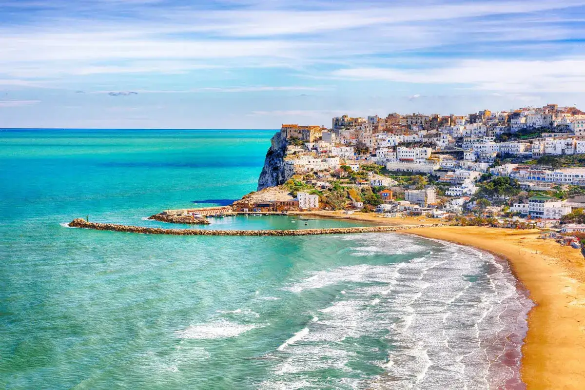 La spiaggia di Procida, con le sue case bianche arroccate sulla scogliera, si affaccia su un mare turchese e cristallino.