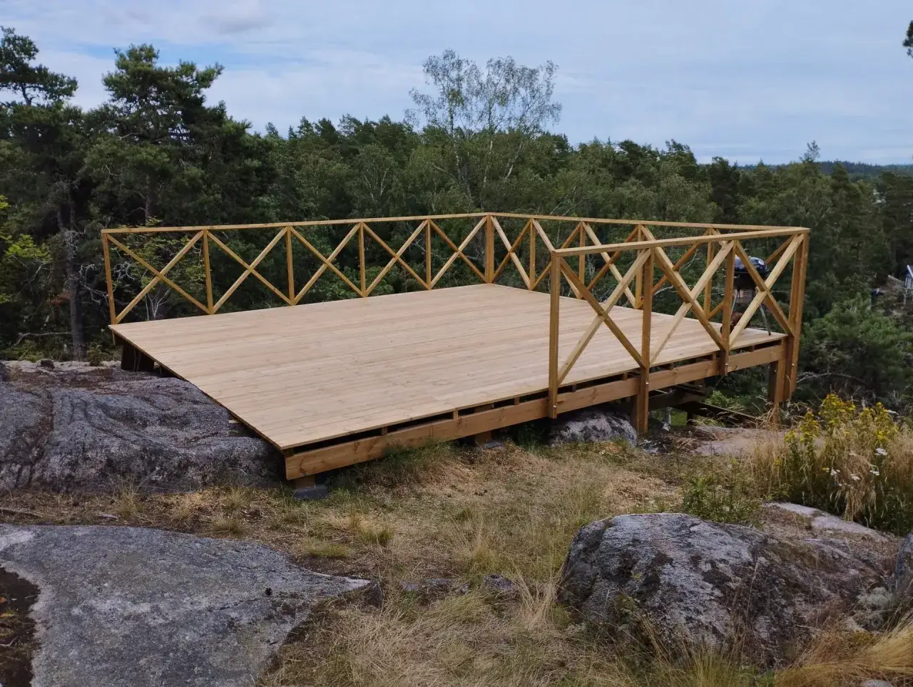 Nybyggd altan i tr&auml; med vackert r&auml;cke, placerad p&aring; en klippa med utsikt &ouml;ver skog. En bra investering f&ouml;r att h&ouml;ja v&auml;rdet p&aring; huset, funderar du p&aring; bygga altan kostnad?