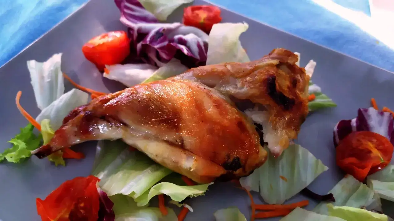 Un succulento coniglio allo spiedo, dorato e croccante, servito su un letto di insalata fresca con pomodorini e carote julienne.