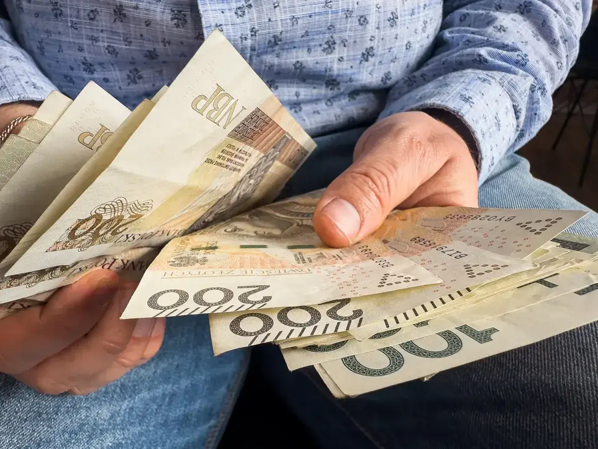 Ręce trzymające polskie banknoty 200 zł i 100 zł. Zastanawiasz się, kiedy najlepiej przejść na emeryturę w 2026 roku?