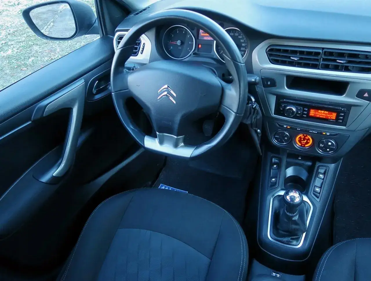 Wnętrze Citroen C-Elysée: kierownica, deska rozdzielcza z radiem i nawiewami, dźwignia zmiany biegów i fotel kierowcy.