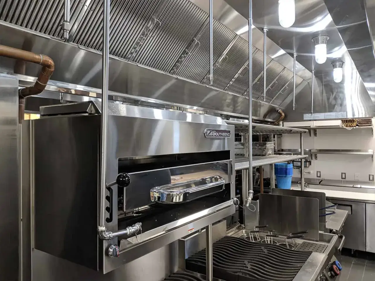Une cuisine professionnelle moderne avec un four à pizza Southbend et une friteuse, sous une grande hotte aspirante en acier inoxydable.