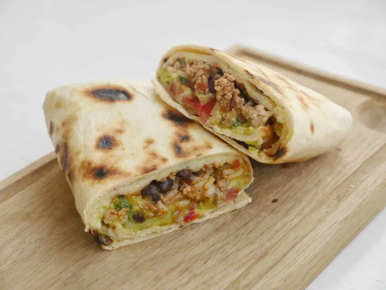 Två halverade burritos de carne med köttfärs, bönor, ris och grönsaker på en träskärbräda.