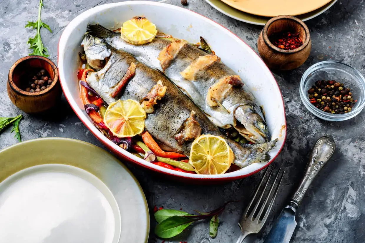 Deux truites entières rôties avec des citrons et des légumes, prêtes pour une délicieuse recette truite.
