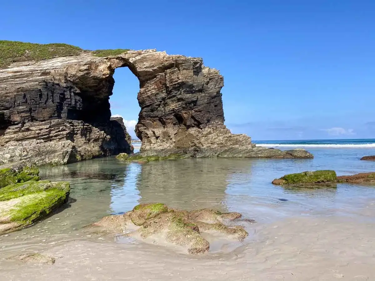 Felsentor am Praia das Catedrais, das wie eine Kathedrale wirkt. T&uuml;rkises Wasser und gr&uuml;ne Algen auf den Felsen.