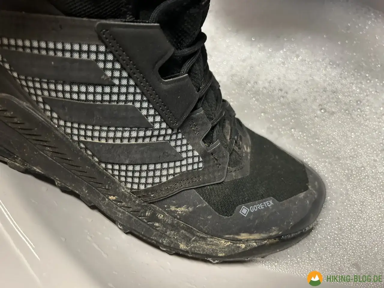 Schmutziger adidas Terrex Schuh im Schaumbad, bereit für die Waschmaschine.