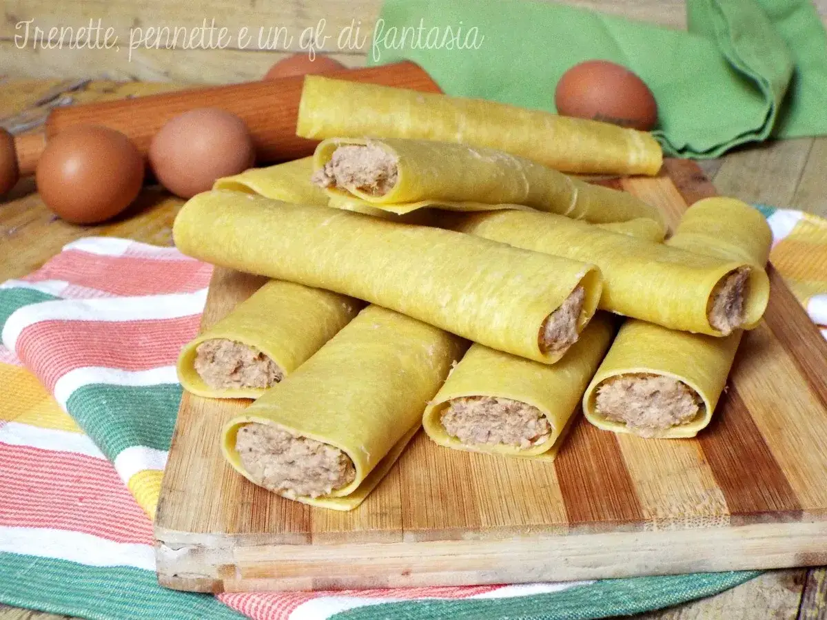 Cannelloni di carne ricetta della nonna pronti per essere cotti, con uova e un mattarello sullo sfondo.