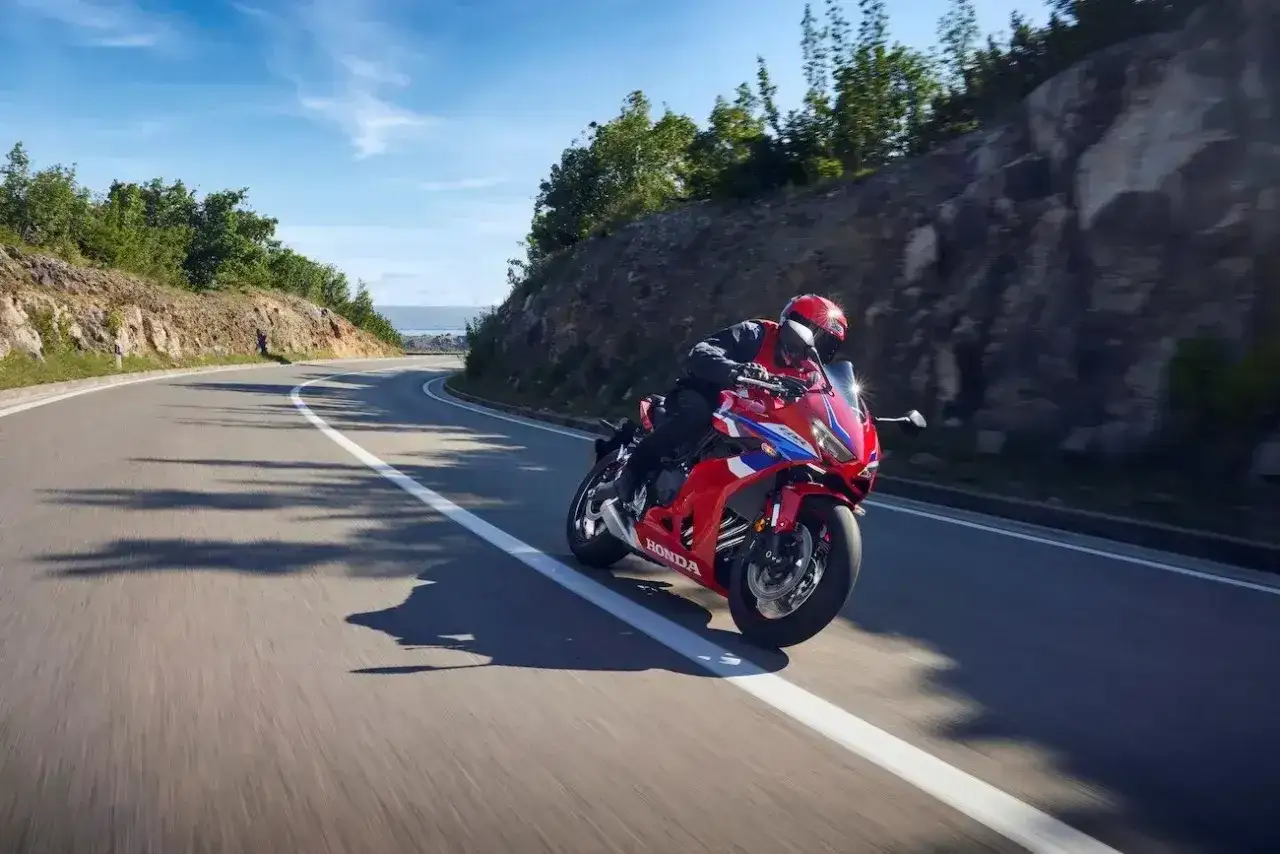 Czerwony motocykl Honda CBR 650 z kierowcą w kasku pokonuje zakręt na malowniczej drodze przybrzeżnej.