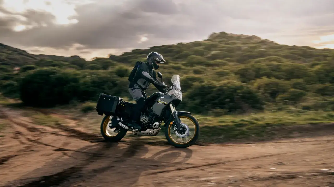 Motocyklista na Tenere 700 przemierza piaszczystą drogę wśród wzgórz.