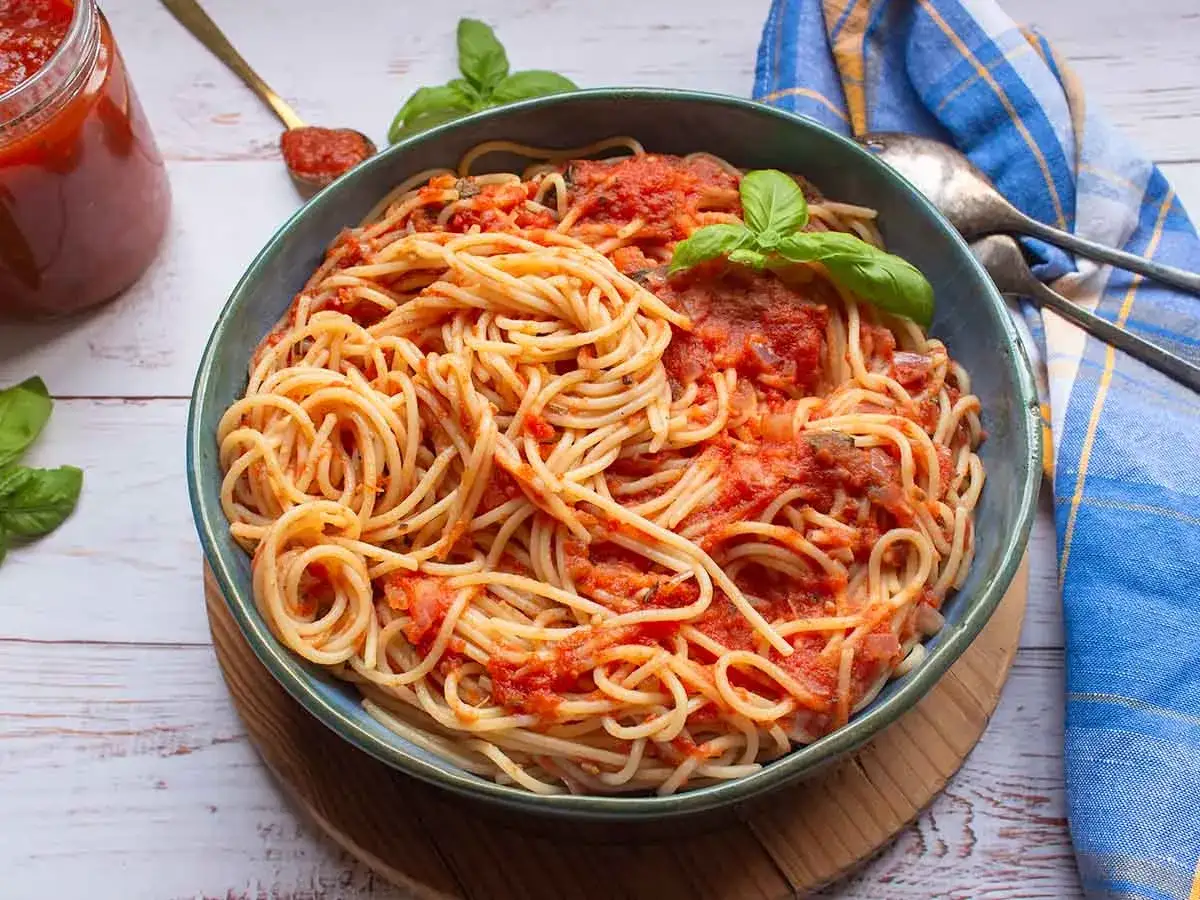 En skål med spaghetti pomodoro, toppad med färsk basilika. En burk tomatsås och en sked syns i bakgrunden.