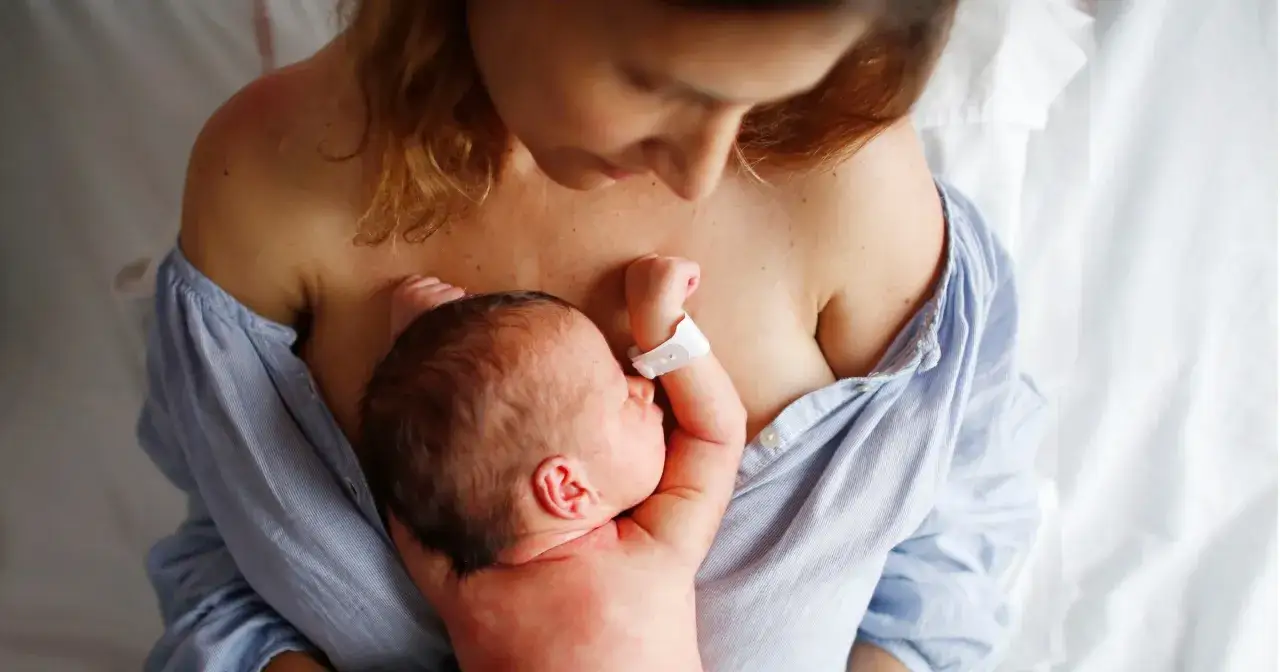 Mama tuli tuli noworodka, czule go obejmuje. To piękny okres po porodzie, pełen miłości i bliskości.