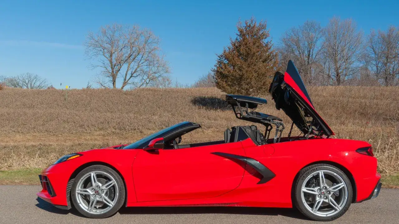 Czerwony Chevrolet Corvette C8 z otwartym dachem, gotowy na przejażdżkę po malowniczej drodze wśród suchych traw i drzew.