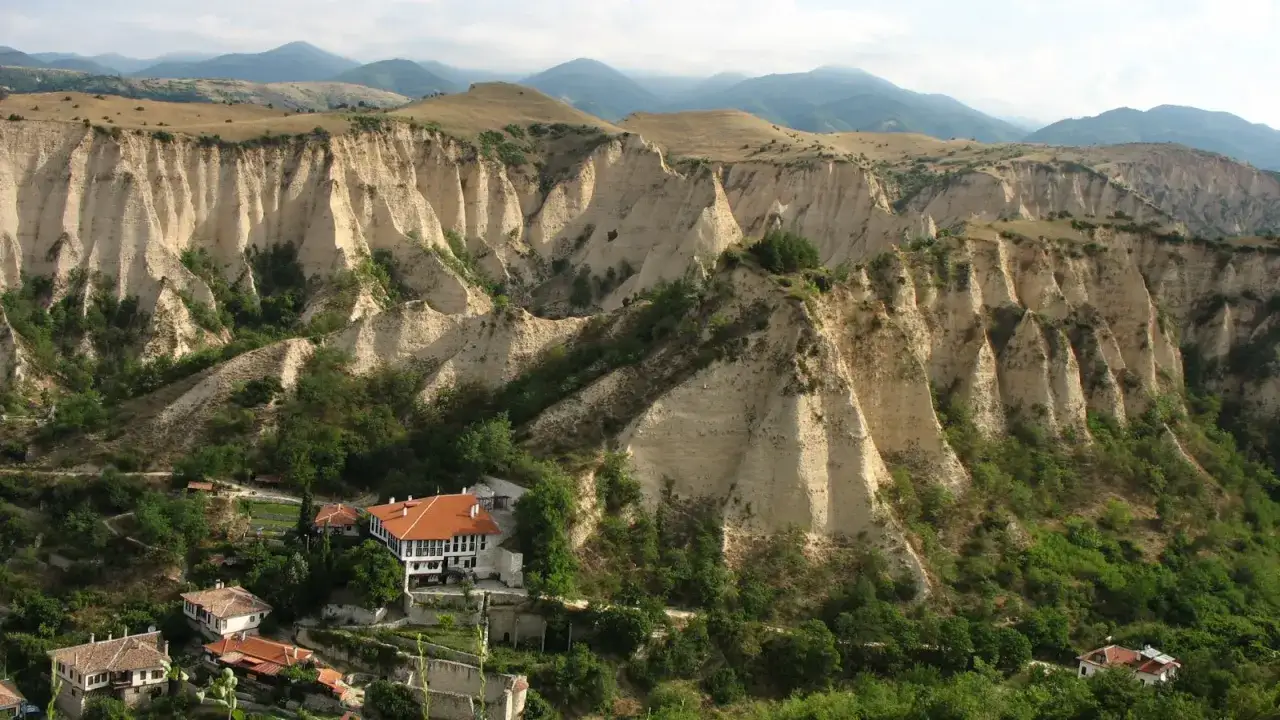 Beeindruckende Sandsteinformationen im Gebirge in Bulgarien, mit traditionellen H&auml;usern am Fu&szlig;e der Erosionslandschaft.