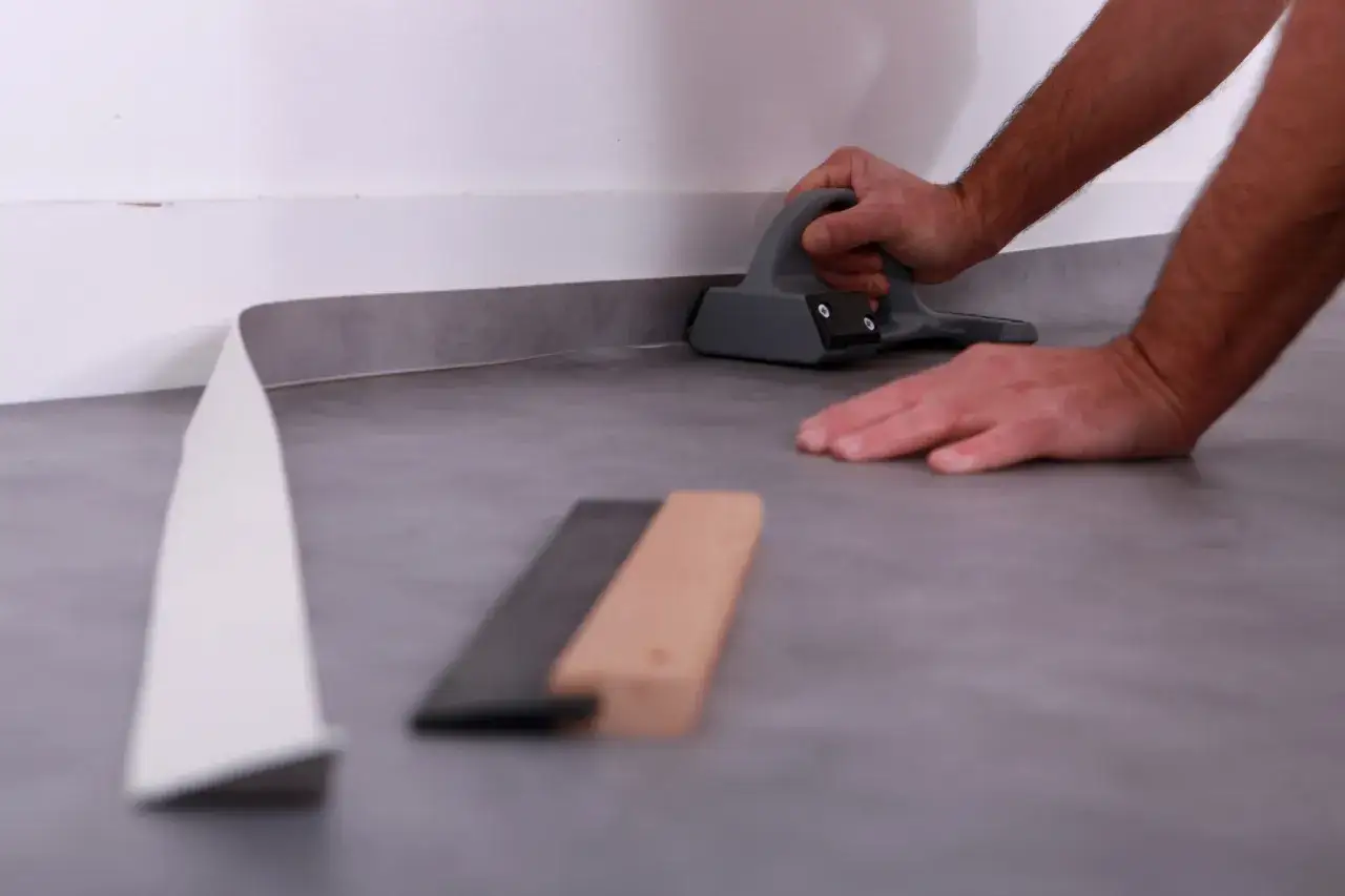 Main tenant utilise un outil pour bien comment poser du lino contre le mur.