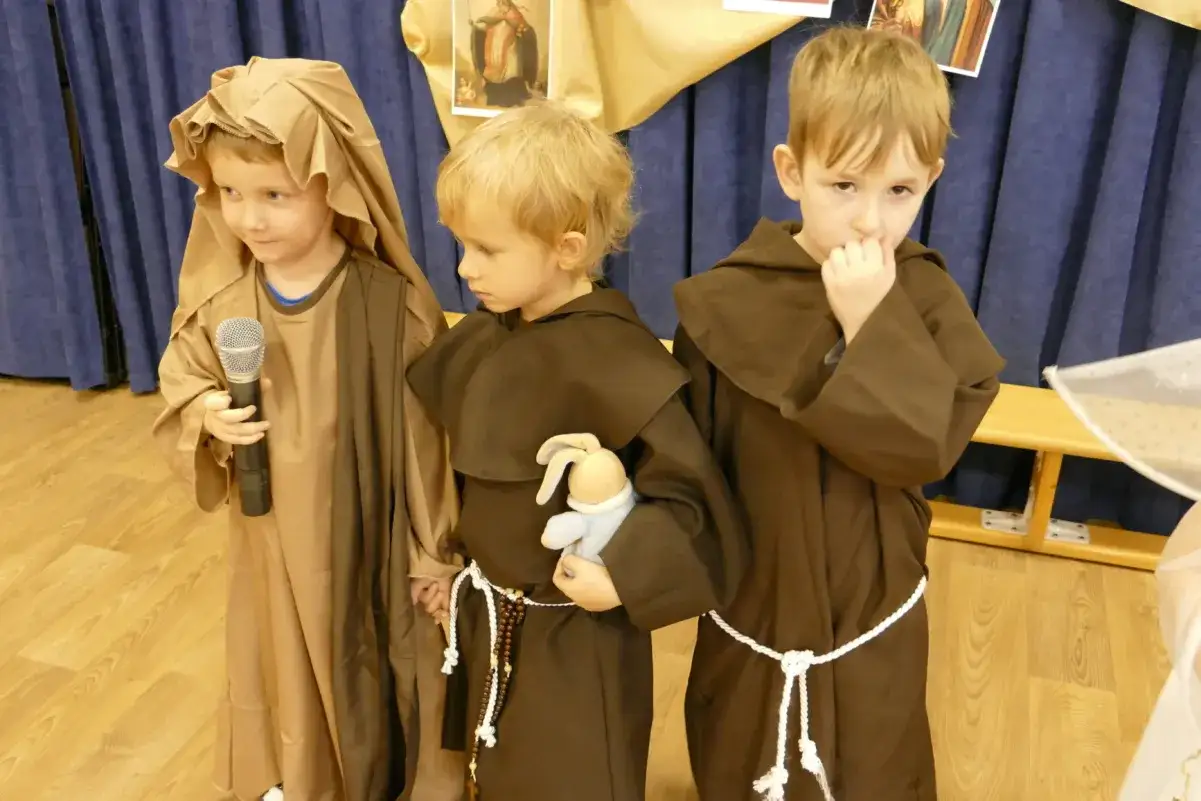 Trzech chłopców w strojach świętych. Jeden trzyma mikrofon, drugi pluszowego zajączka.