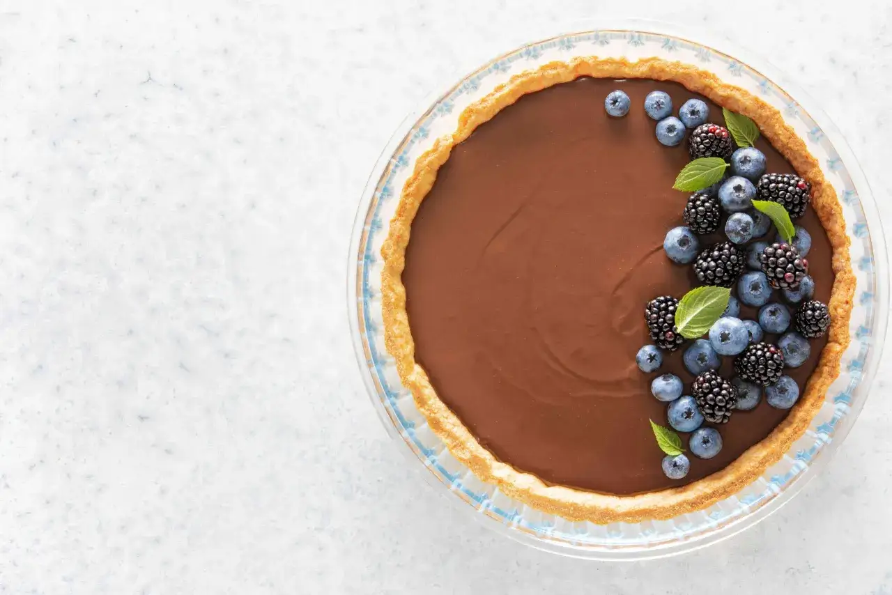 Une délicieuse tarte au chocolat au lait, garnie de myrtilles et de mûres fraîches, prête à être dégustée.
