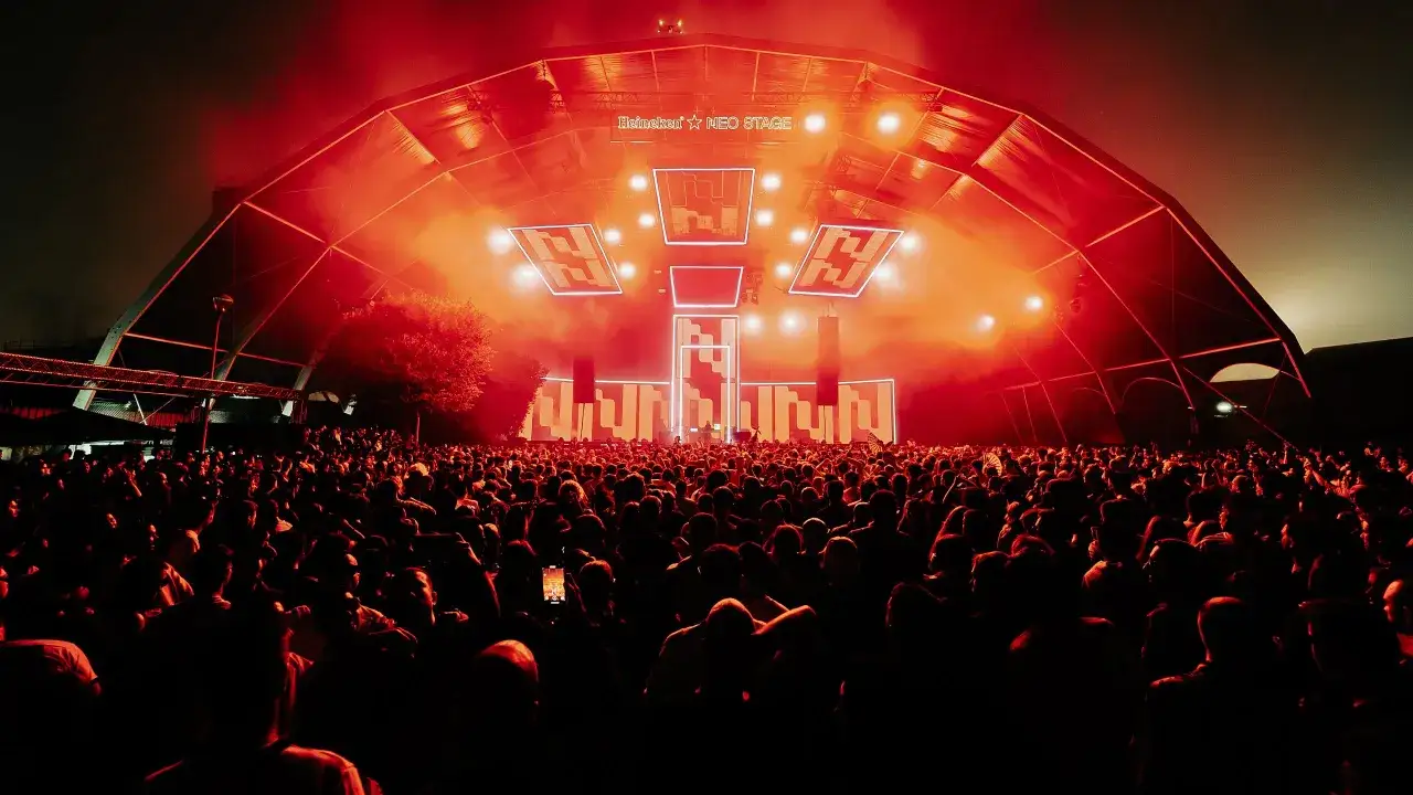 Folla in delirio sotto un palco illuminato di rosso, pronto per il **best techno dj**. Luci al neon e fumo creano un'atmosfera elettrica.