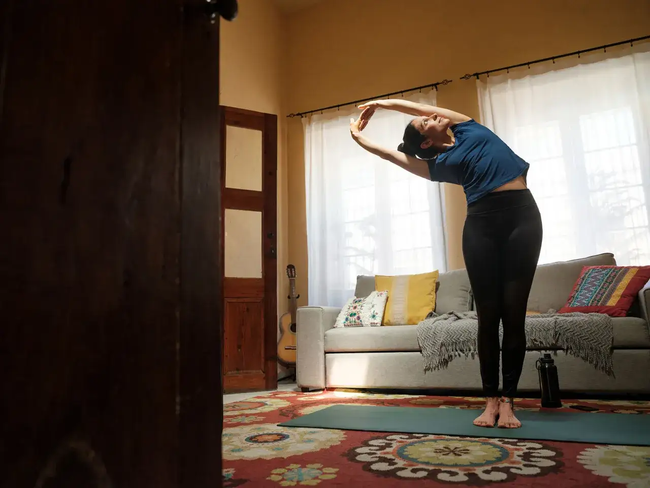 Mujer estir&aacute;ndose en una esterilla, practicando t&eacute;cnicas de relajaci&oacute;n en su sala.
