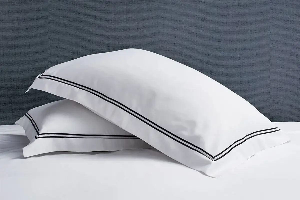 Two white pillow shams with black trim are stacked. The size of a standard pillow sham is typically 20x26 inches.