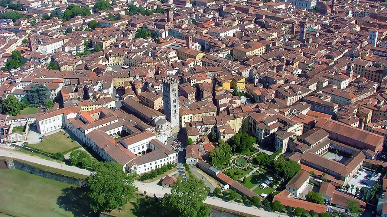 Vue a&eacute;rienne de Lucca, avec ses toits de tuiles rouges et la tour Guinigi. Un parking est visible pr&egrave;s de la cath&eacute;drale.