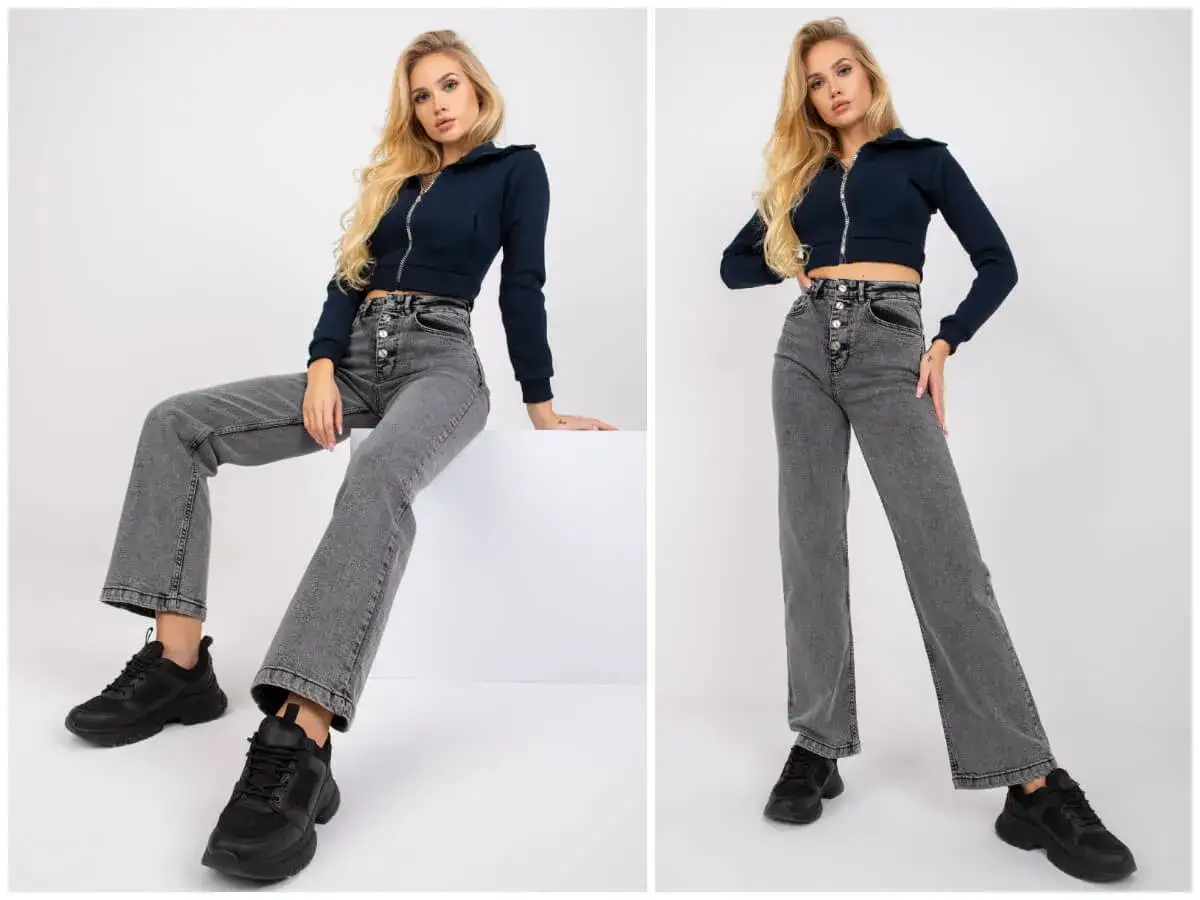 Blondynka w granatowej bluzie i szarych spodniach wide leg, które rozszerzają się ku dołowi.