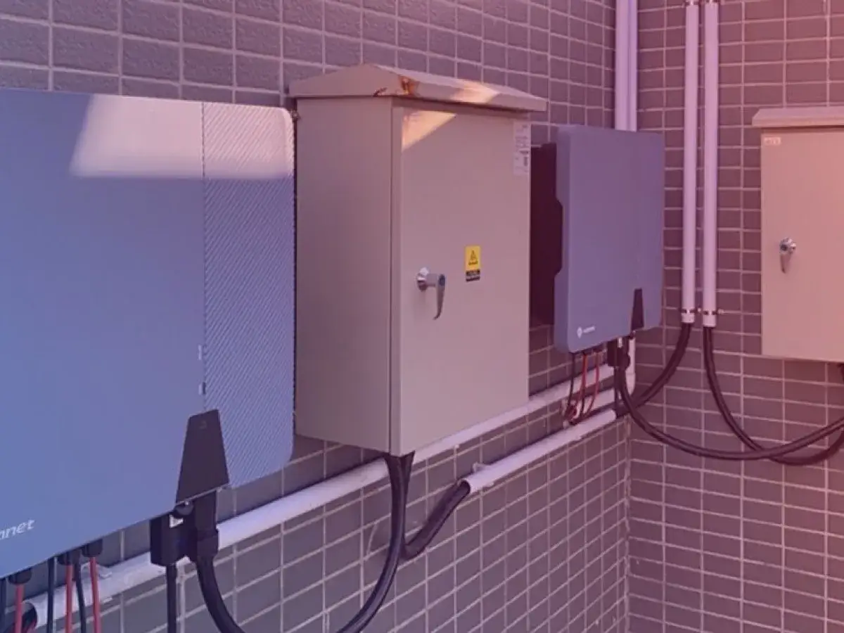 Instalacja fotowoltaiczna z kilkoma skrzynkami i przewodami na tle kafelkowej ściany.