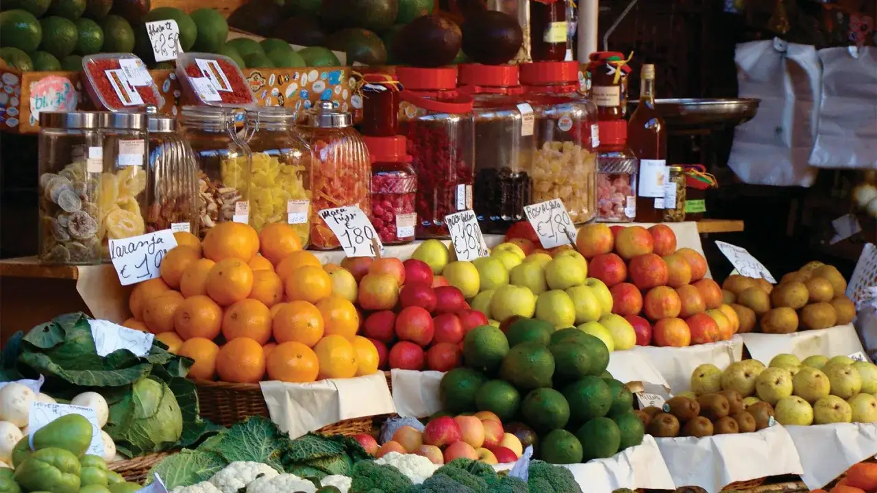Bunter Obst- und Gemüsestand auf dem Mercado dos Lavradores mit Orangen, Äpfeln, Kiwis, Kohl und eingelegten Früchten.