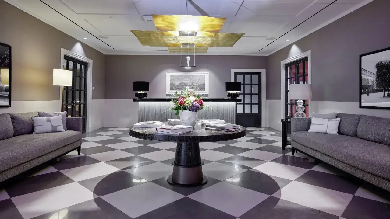 Elegante **priority lounge** mit Schachbrettboden, zwei Sofas, einem runden Tisch mit Blumen und Büchern sowie einer Rezeption.