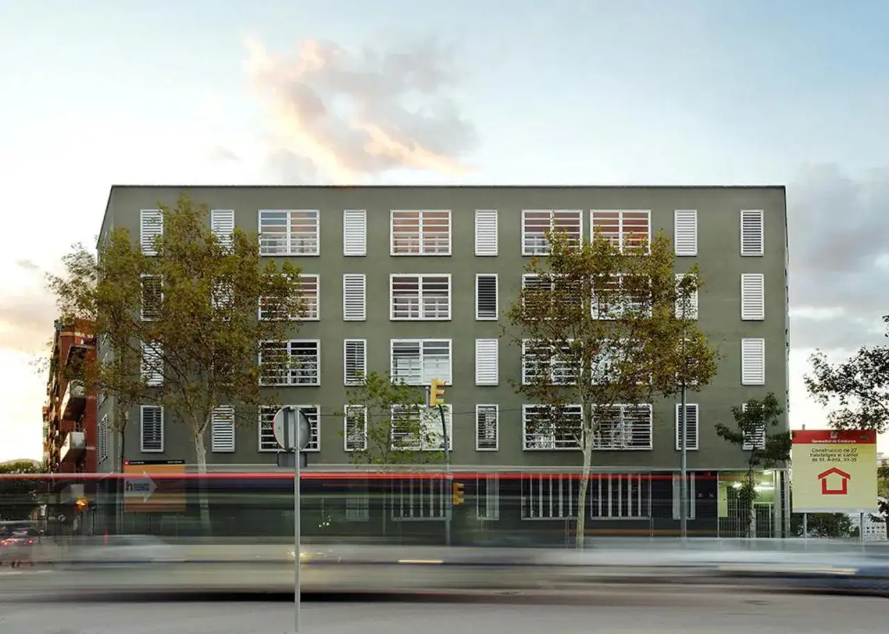Edificio de pisos de protecci&oacute;n oficial en Barcelona, promovido por La Caixa. Fachada gris con ventanas blancas y persianas.