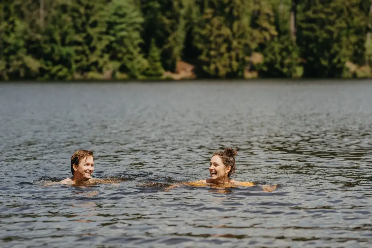 Ein Paar genießt das kühle Wasser eines **Badesee Harz** an einem sonnigen Tag, umgeben von grünen Bäumen.