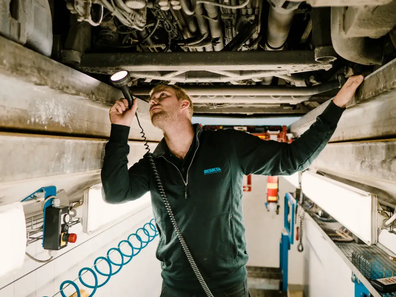 Mekaniker inspekterar bilens undersida med ficklampa. Han ser ut att fundera på om kan man besikta bilen tidigare.