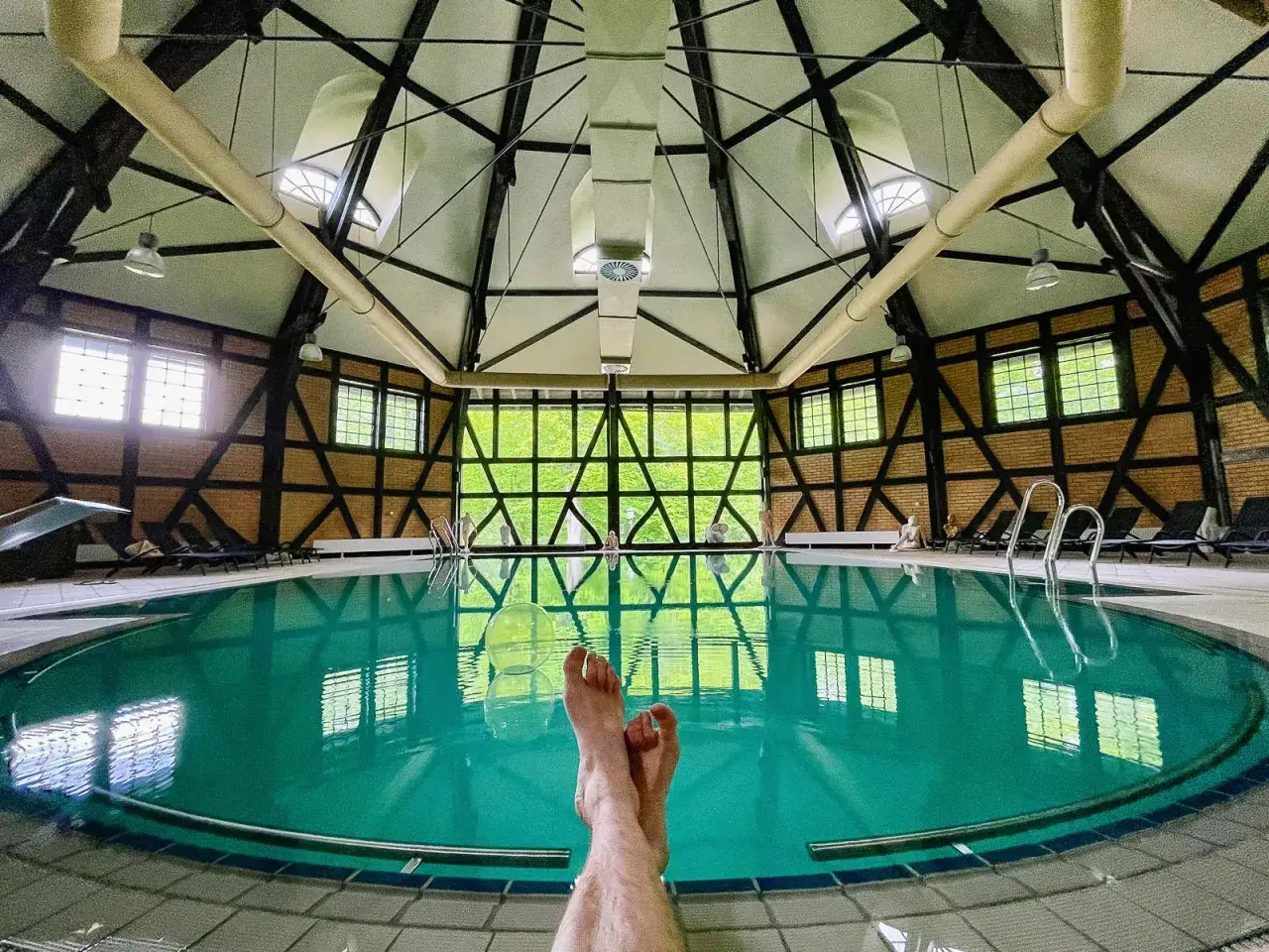 Relaks przy basenie w Zamek Kliczków. Woda w basenie odbija światło i architekturę z charakterystyczną więźbą dachową.