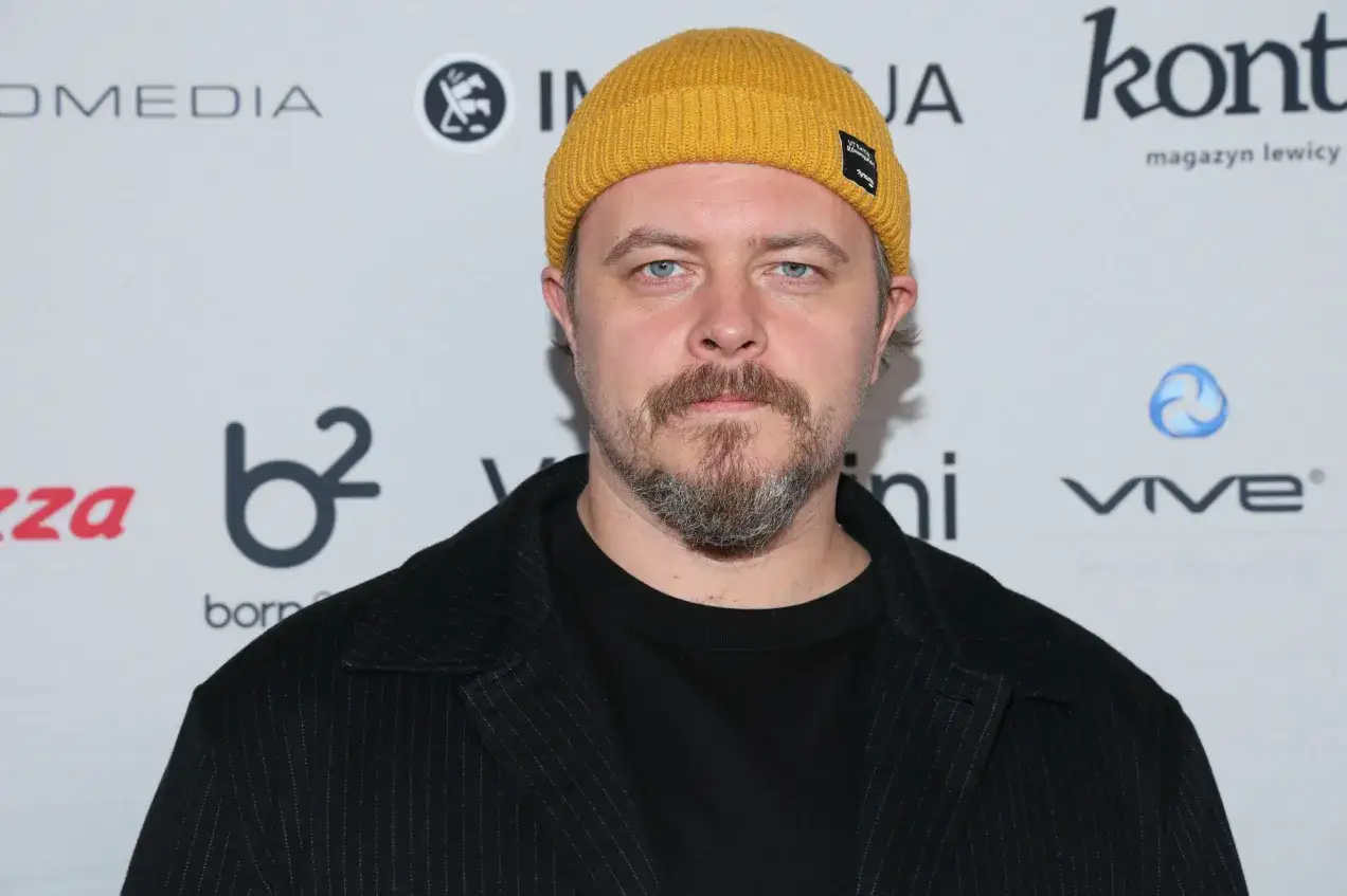 Tomasz Schuchardt, znany z wielu filmów, seriali i programów, w żółtej czapce i czarnym stroju.