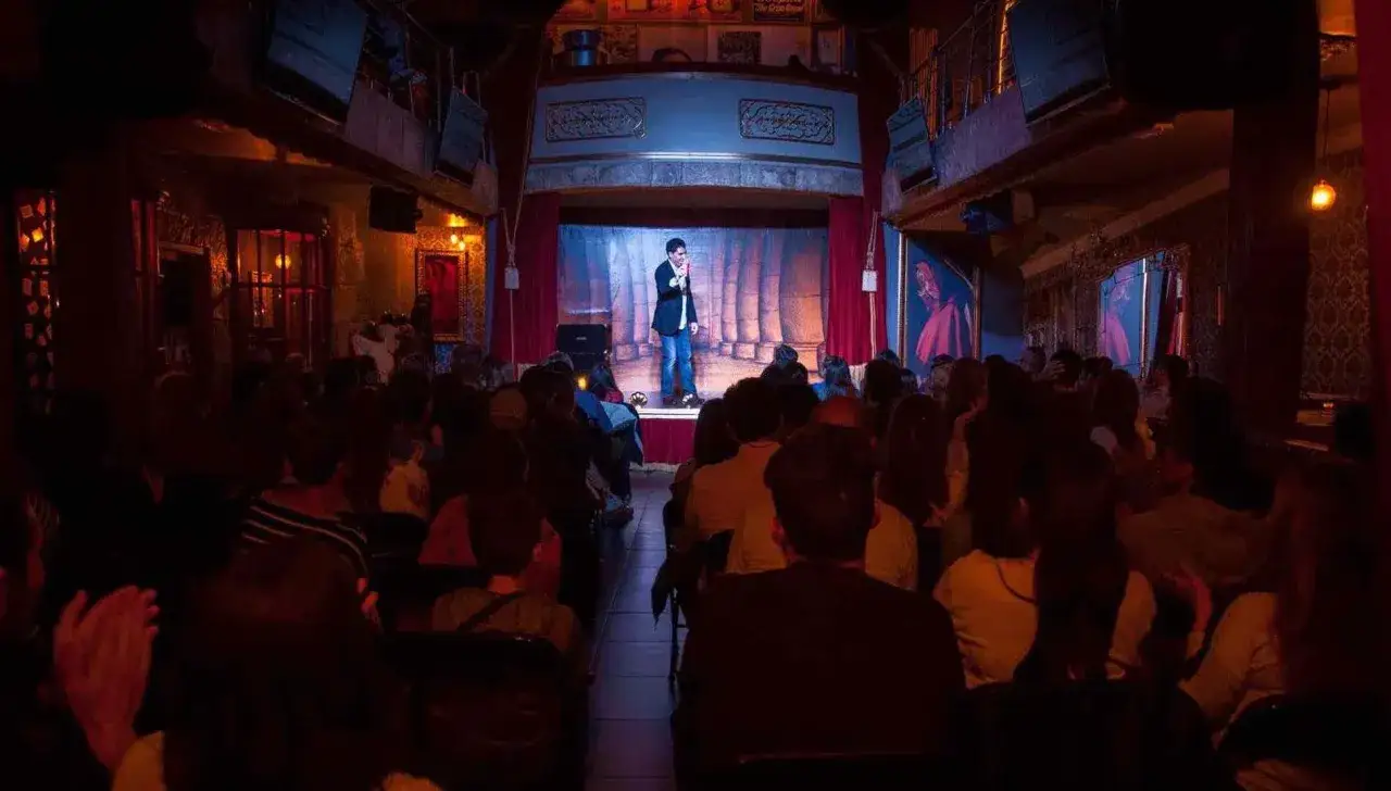 Un mago act&uacute;a en un escenario ante un p&uacute;blico en el **magic museum Pe&ntilde;&iacute;scola**. La sala tiene una decoraci&oacute;n teatral y oscura.