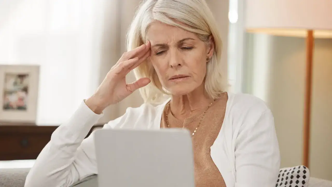 Besorgte Frau mit Hand an der Stirn, die einen Online-Demenztest am Laptop macht.