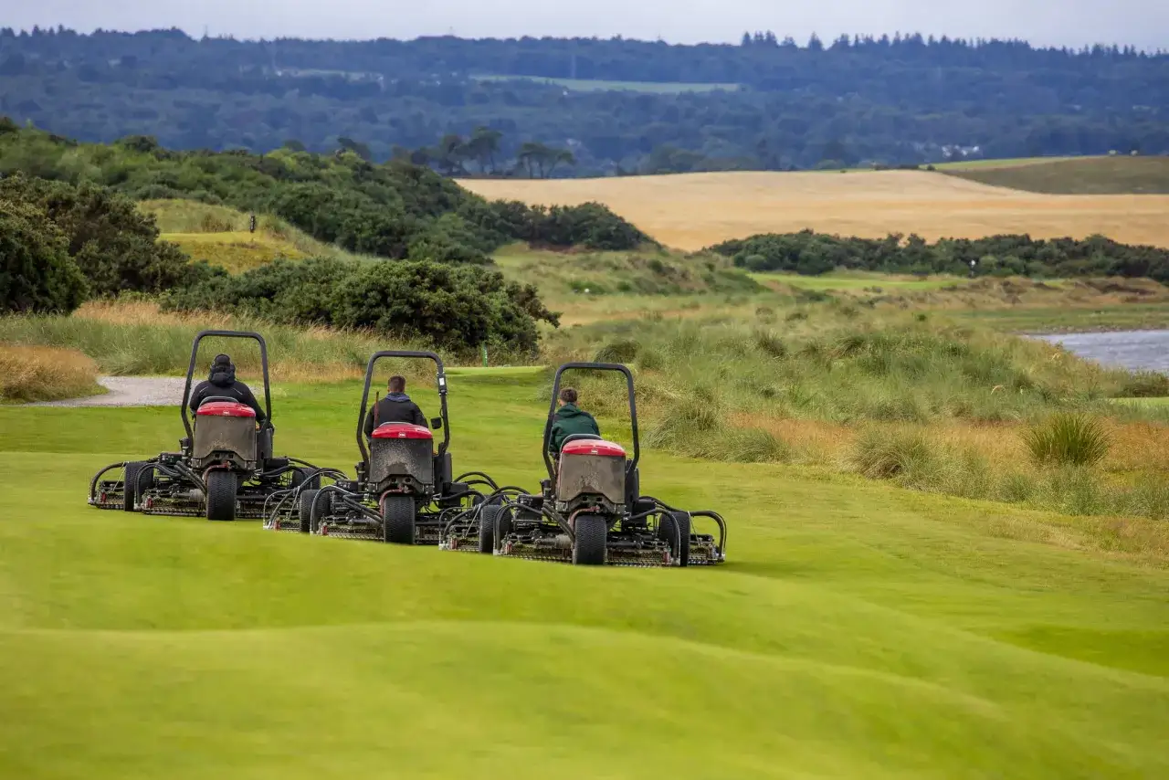 Trzech greenkeeper&oacute;w w pracy, koszących trawę na polu golfowym.