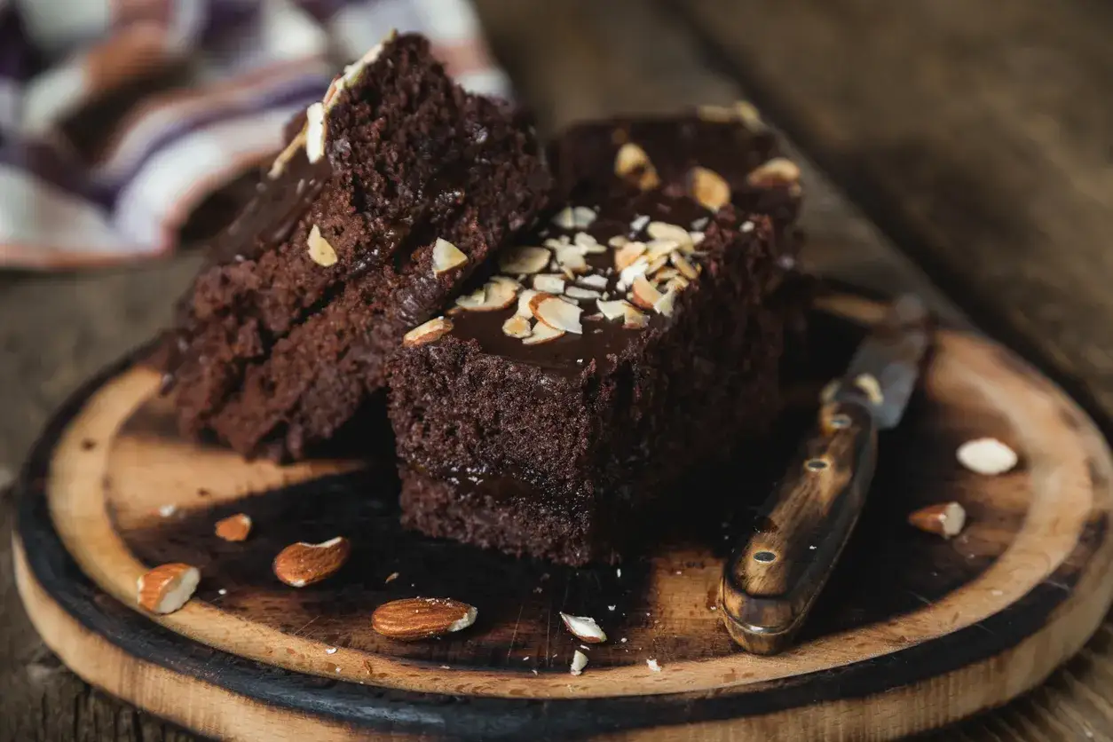 Pyszne brownie z fasoli, polane czekoladą i posypane migdałami, leżą na drewnianej desce.