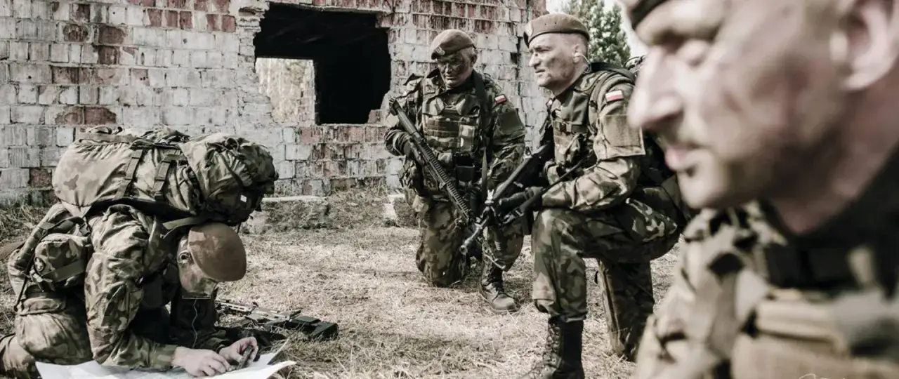 Żołnierze wojsk obrony terytorialnej w kamuflażu analizują mapę przy zrujnowanej ścianie.