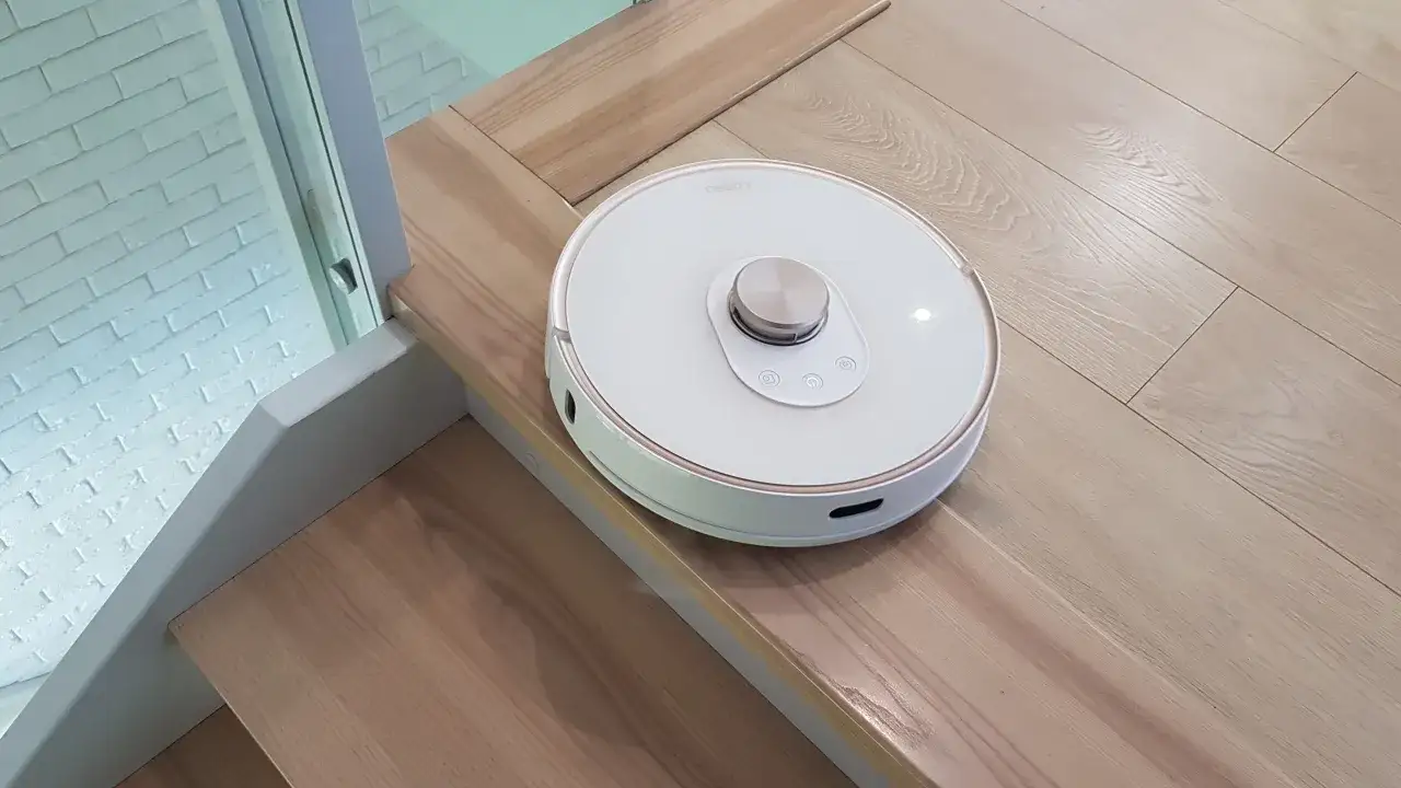 Biały robot sprzątający na drewnianych schodach. Czy roboty sprzątające z funkcją mopowania to tylko chwyt marketingowy?