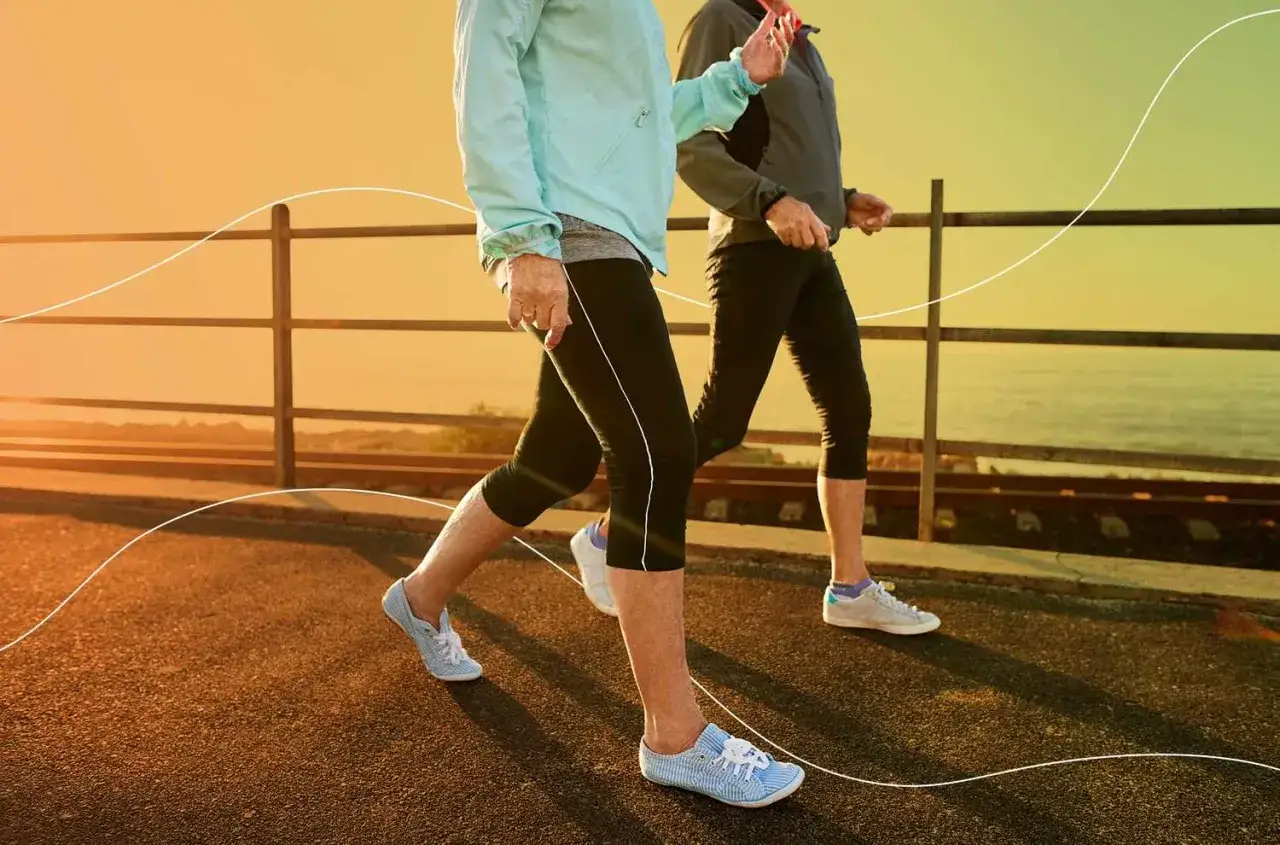 Dwie osoby w sportowych ubraniach spacerują brzegiem morza. Codzienne chodzenie 5 km dziennie efekty widać w ich dobrej kondycji.