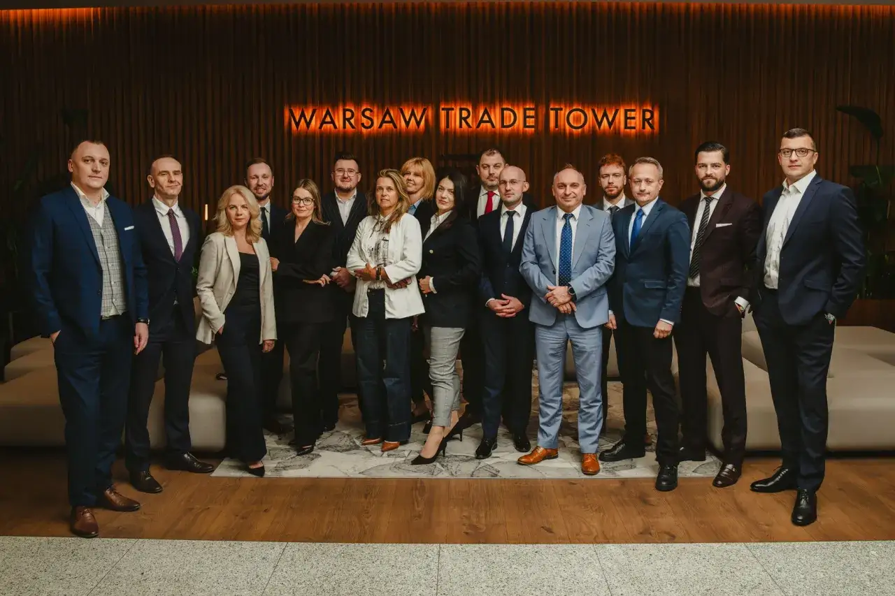 Grupa profesjonalistów w garniturach pozuje przed napisem
