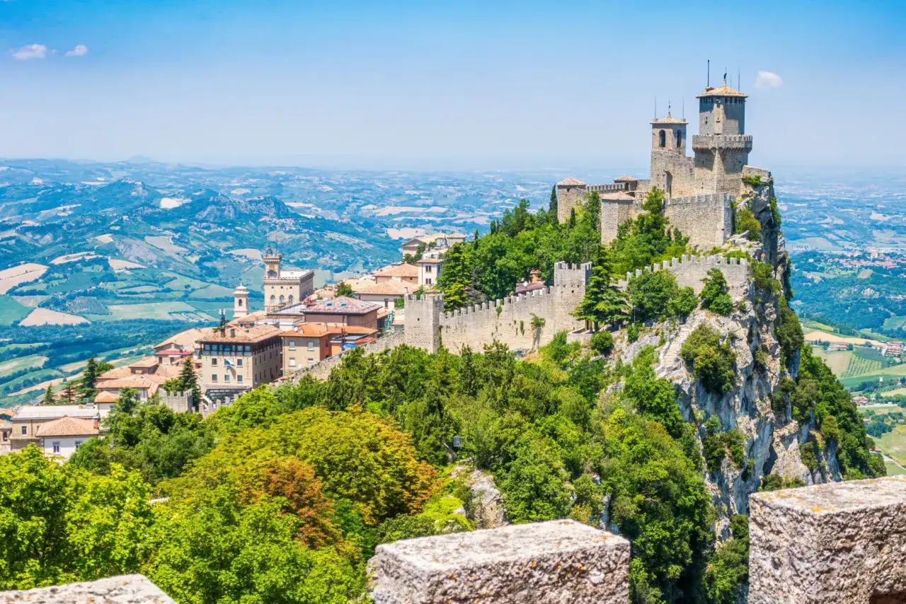 San Marino, enklawa na terytorium Włoch, z górującymi wieżami zamku na skalistym szczycie, otoczona zielonymi wzgórzami.