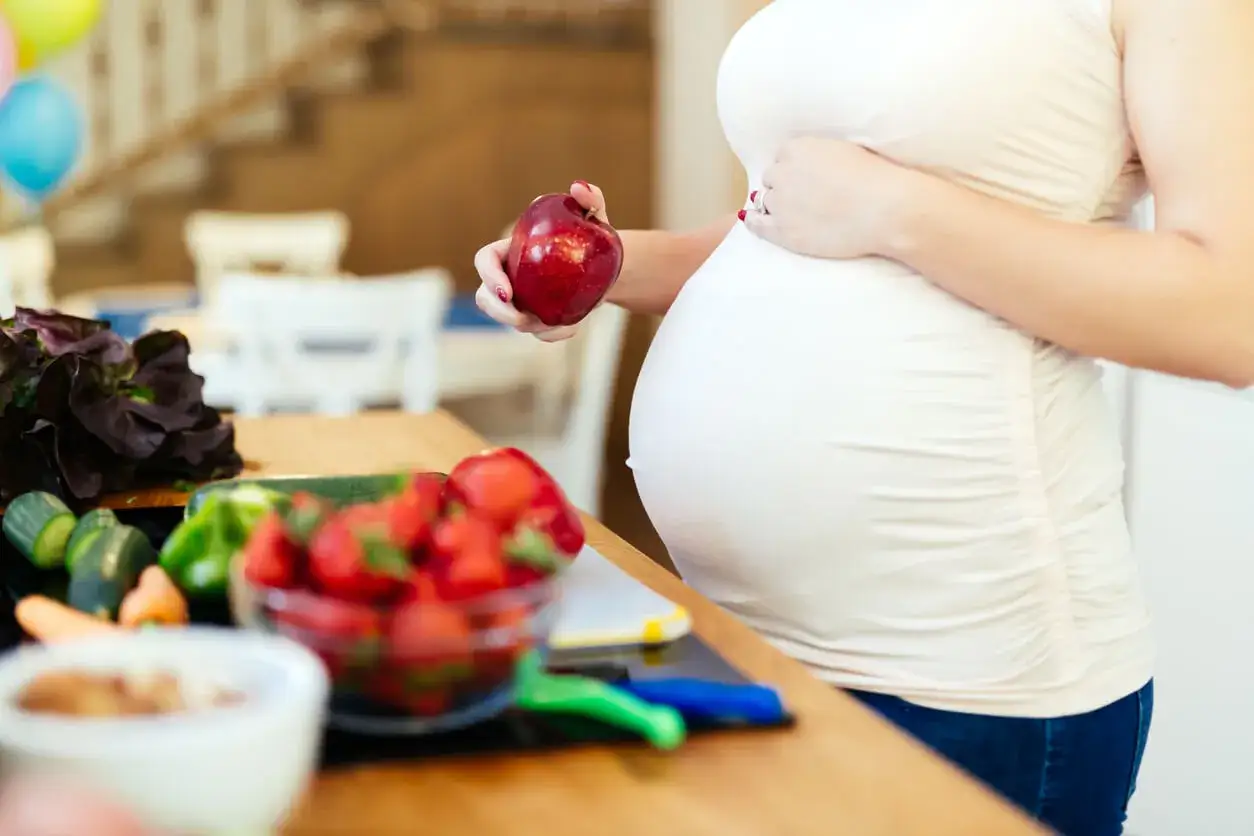Schwangere Frau mit Apfel und frischem Obst. Informiert sich &uuml;ber, wieviel Magnesium in der Schwangerschaft wichtig ist.