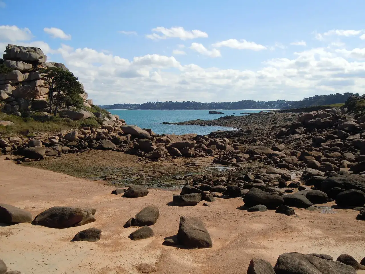 Kamienista plaża nad kanałem La Manche, z formacjami skalnymi i turkusową wodą w tle.