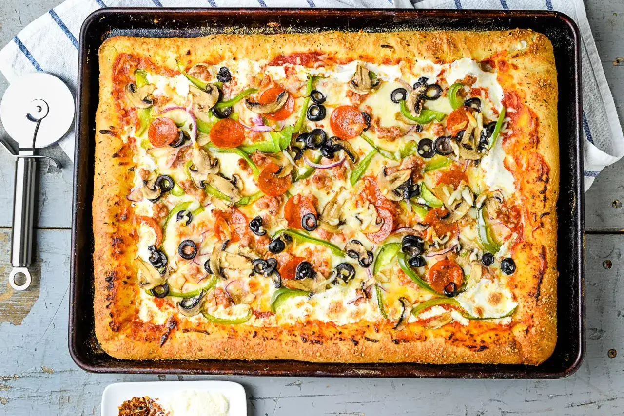 Original italienischer Pizzateig rezept blech: Eine rechteckige Pizza mit Salami, Pilzen, Oliven, Paprika und Zwiebeln auf einem Backblech.