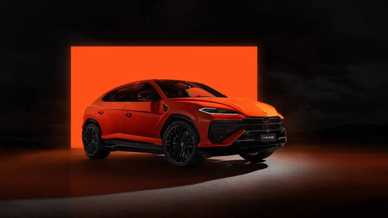 Un imponente **lamborghini urus rojo** se exhibe contra un fondo naranja brillante y un cielo oscuro.