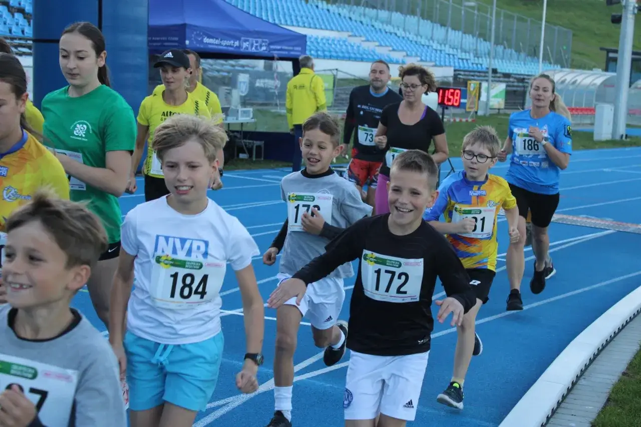Dzieci biegną w zawodach sportowych. Radosne twarze uczestnik&oacute;w test coopera dla dzieci.
