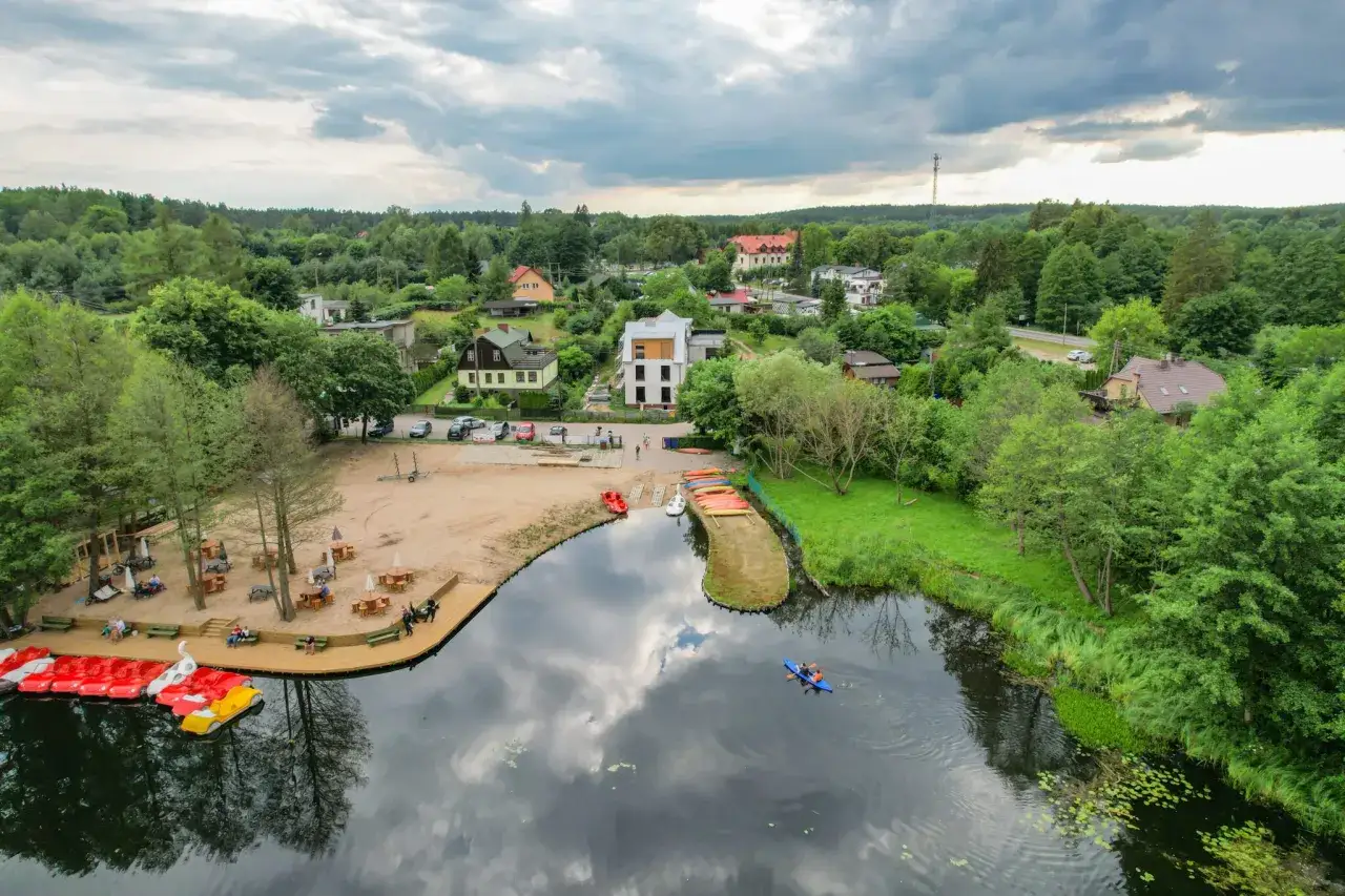 Malownicze Kociewie nad jeziorem, plaża z łódkami i kajakami, domki letniskowe wśród zieleni.