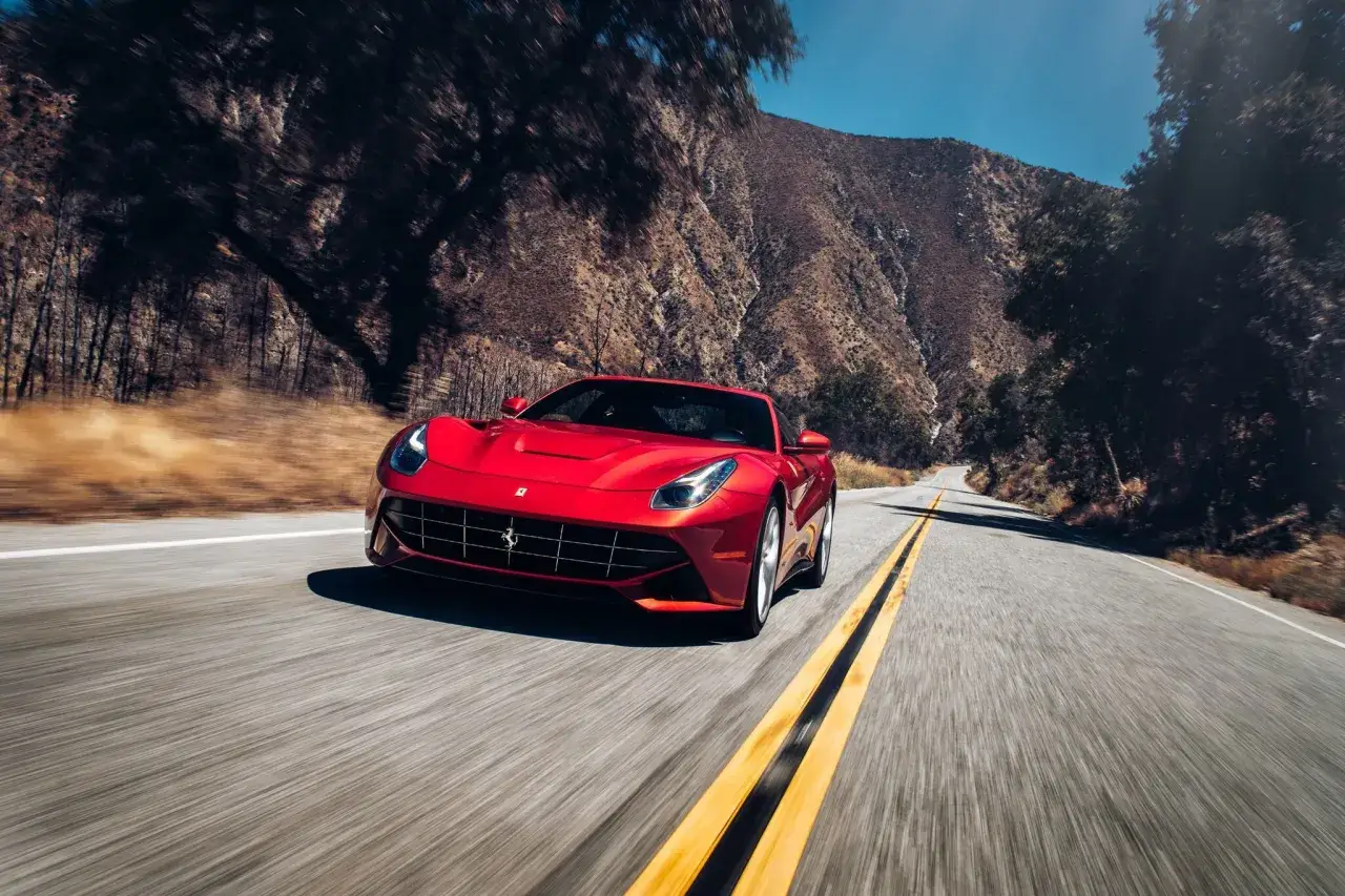 Czerwone Ferrari F12 Berlinetta pędzi krętą drogą przez górzysty, suchy krajobraz.