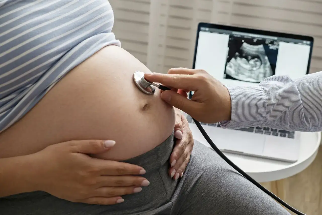 Lekarz osłuchuje brzuch ciężarnej, na ekranie laptopa zdjęcie USG. Ważne, by unikać nieświadome picie alkoholu na początku ciąży.